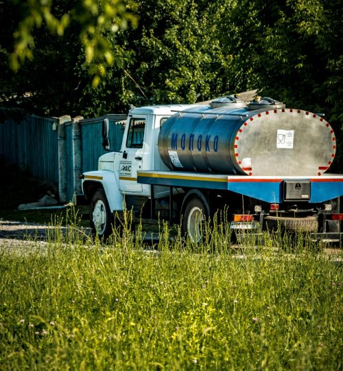 A milk tanker truck in a rural landscape of Sumy Region, Ukraine, surrounded by greenery.
